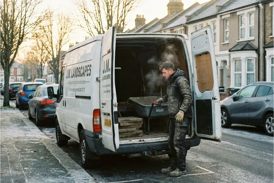 A landscaper loading a wheelbarrow into the back of a work van on a frosty street